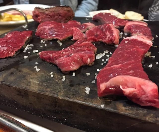 Filetes de carne cruda, condimentados con sal, sobre una tabla de servir de pizarra gris oscura.