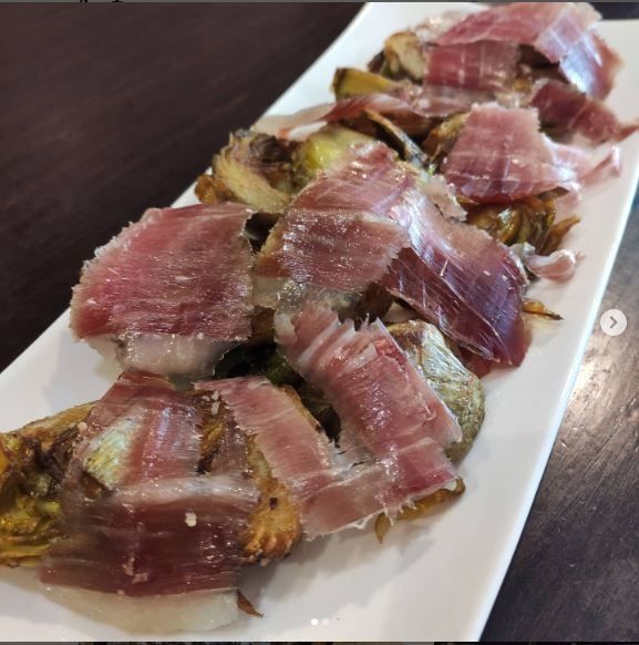 Jamón loncheado y corazones de alcachofa asados ​​sobre un plato rectangular blanco.