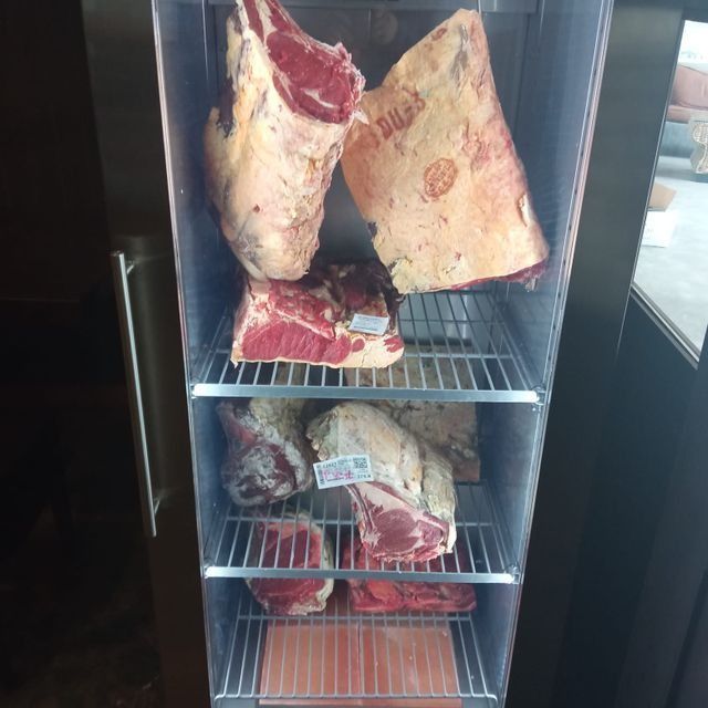 Un refrigerador que exhibe grandes cortes de carne roja cruda, posiblemente madurada en seco.