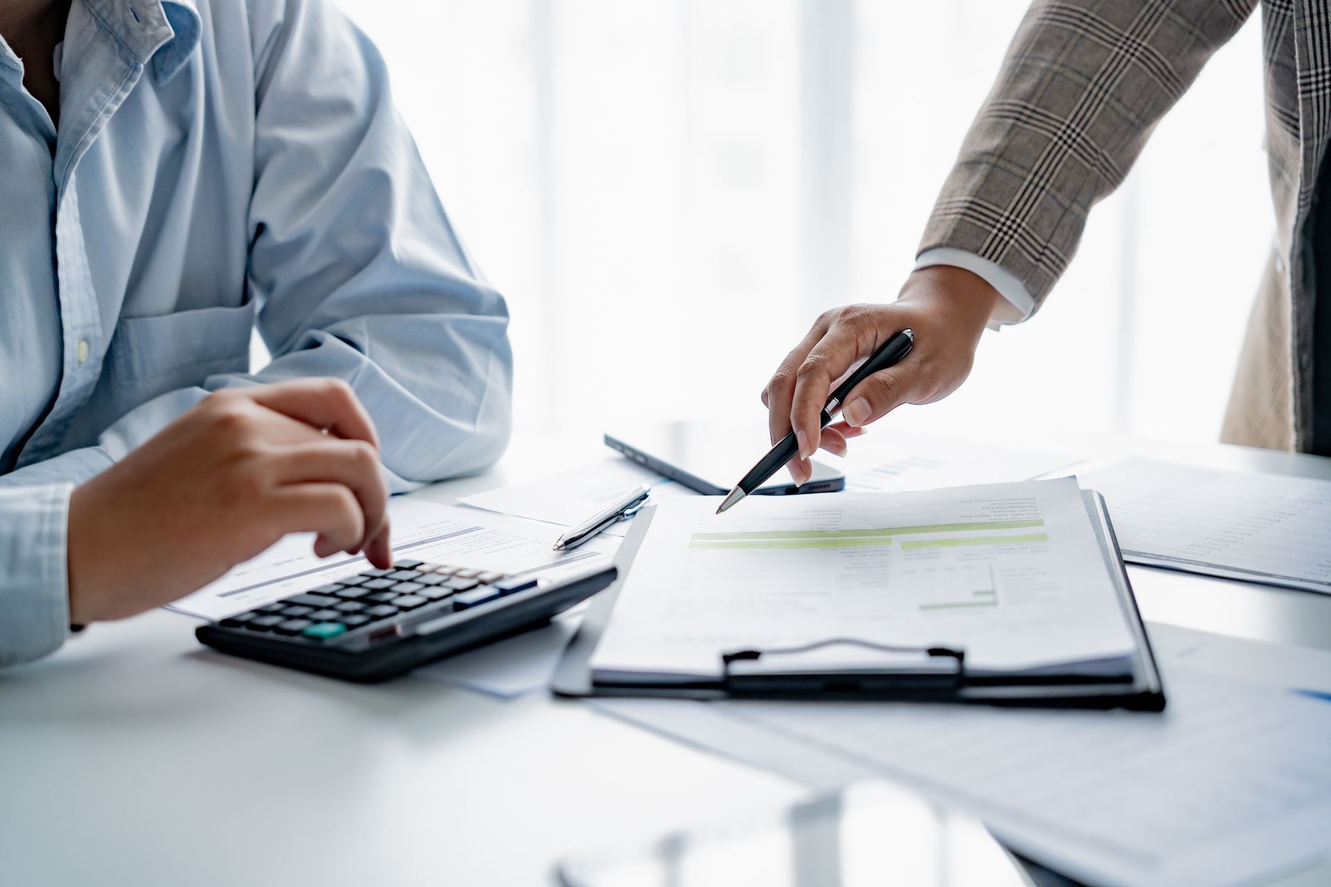 Zwei Personen überprüfen Papierkram mit einem Taschenrechner, eine zeigt auf das Dokument.