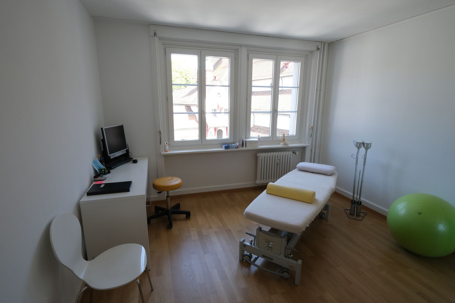 Ein Zimmer mit Bett, Stuhl, Computer und Gymnastikball.