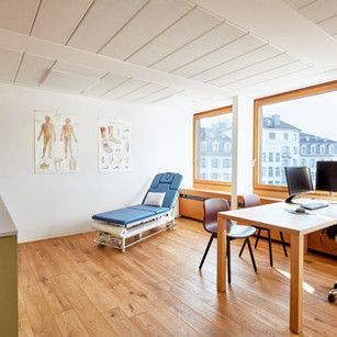 Eine Arztpraxis mit Schreibtisch, Stühlen und Chaiselongue.
