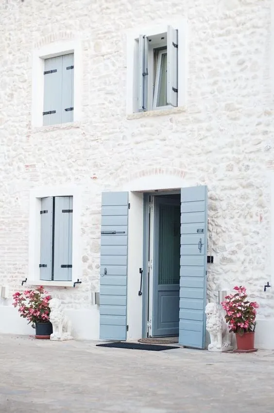 Bâtiment en pierre avec volets battants en bois et porte gris clair.