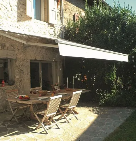 Façade d'une maison avec un store extérieur et une table de jardin en-dessous.
