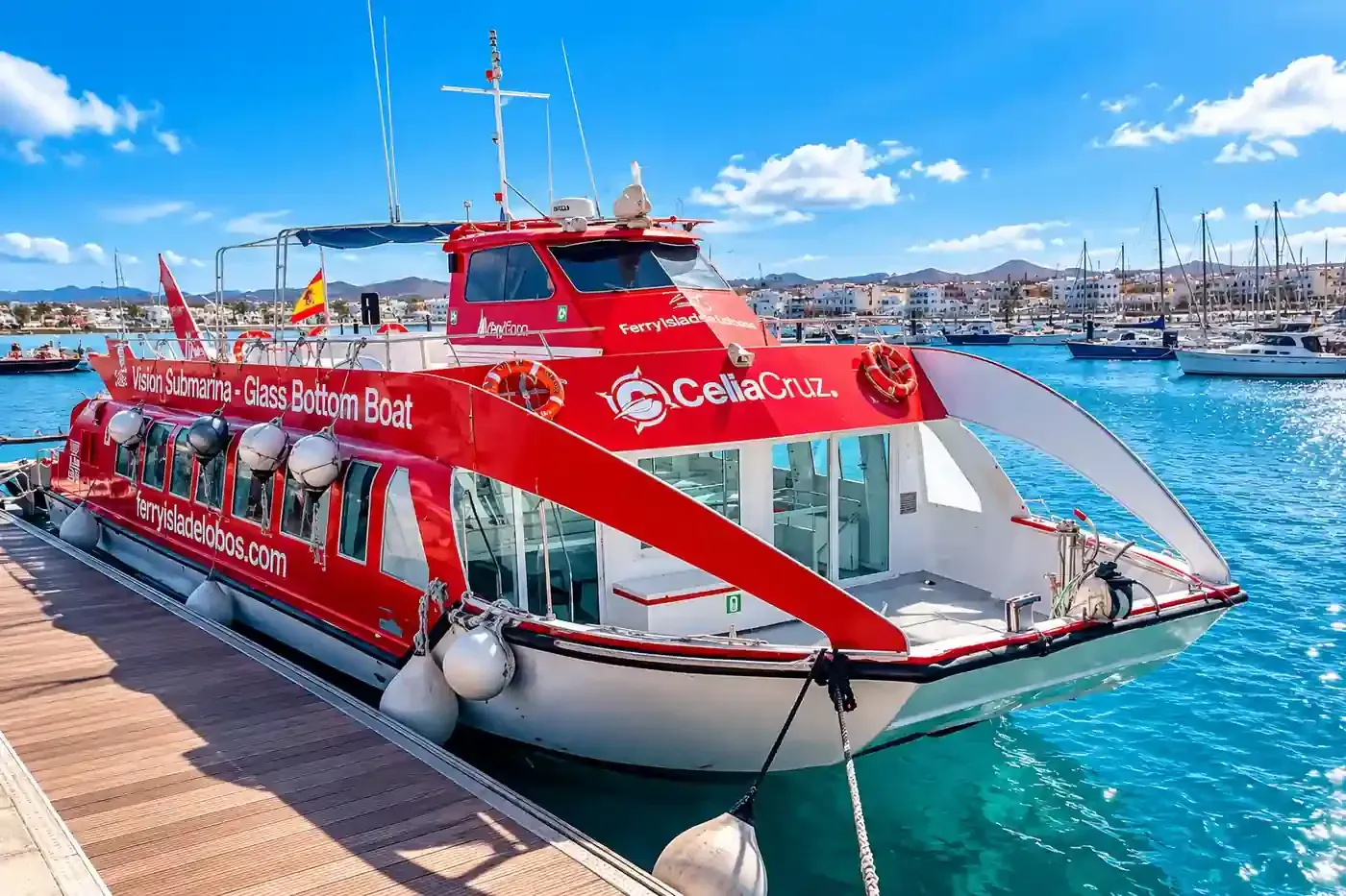 Ferri de pasajeros rojo y blanco atracado en un puerto, con aguas azules y el perfil urbano de la ciudad al fondo