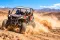 Un buggy todoterreno levantando polvo mientras recorre un camino desértico, con montañas al fondo