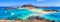 Bahía de color turquesa con veleros, islas arenosas y una colina rocosa bajo un cielo azul brillante