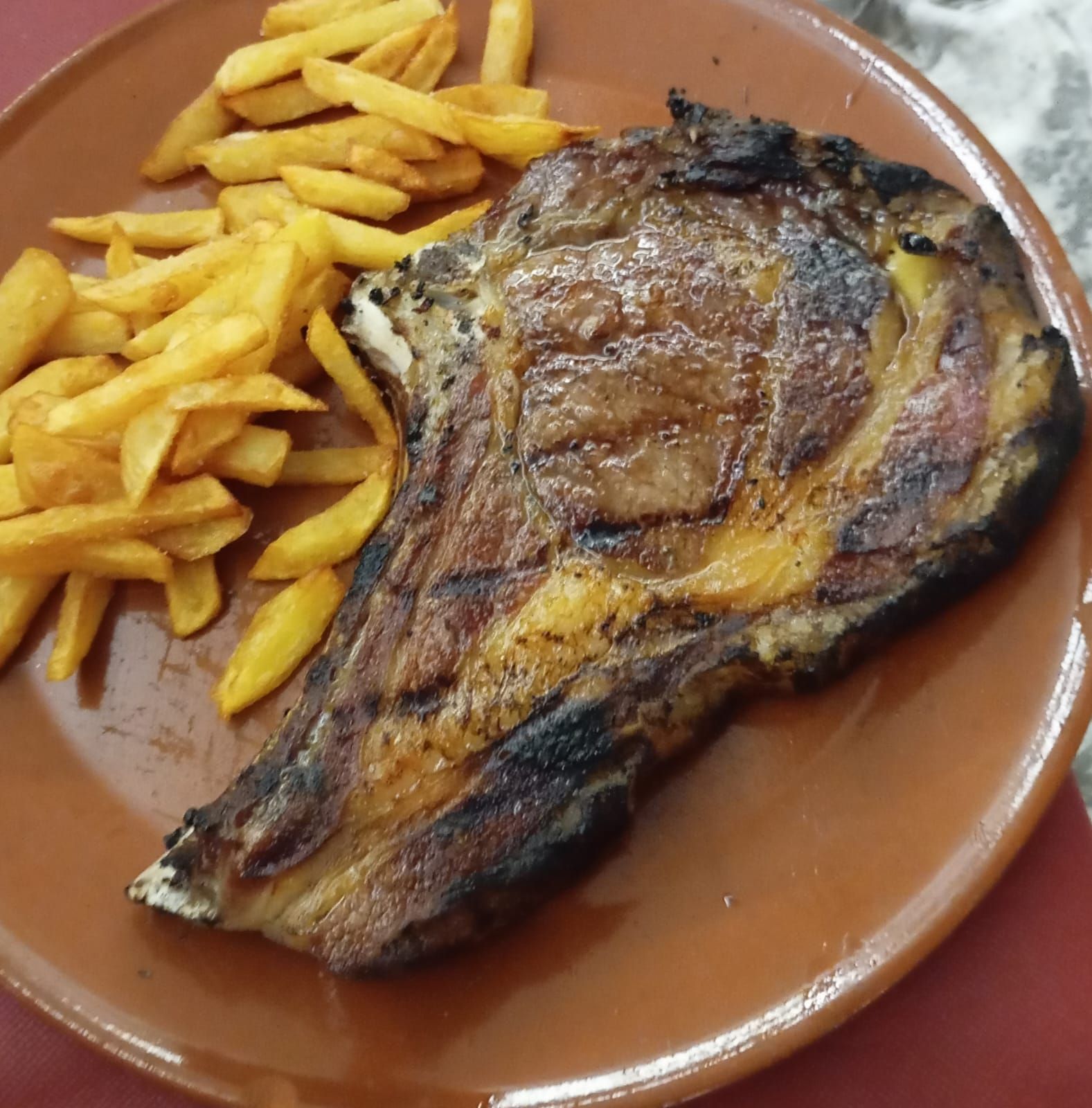 Pescado a la parrilla con papas fritas en un plato marrón.