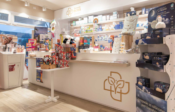 Interno della farmacia con bancone bianco  econ scaffali pieni di prodotti.