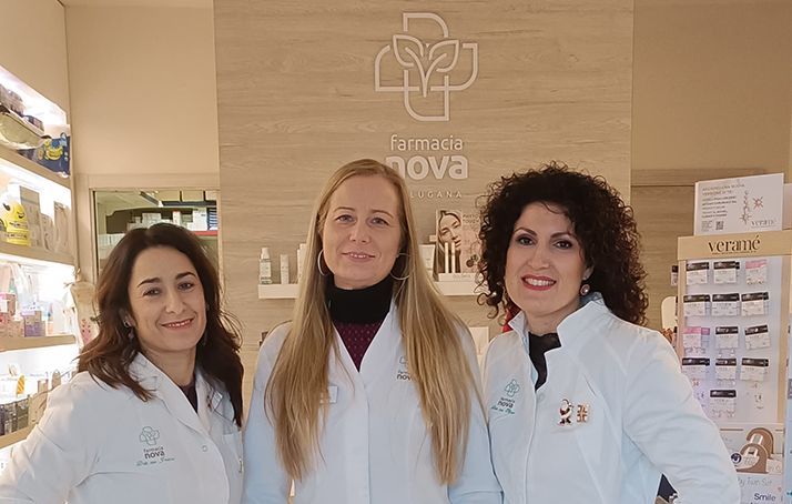 Tre donne in camice in una farmacia, in piedi davanti al logo