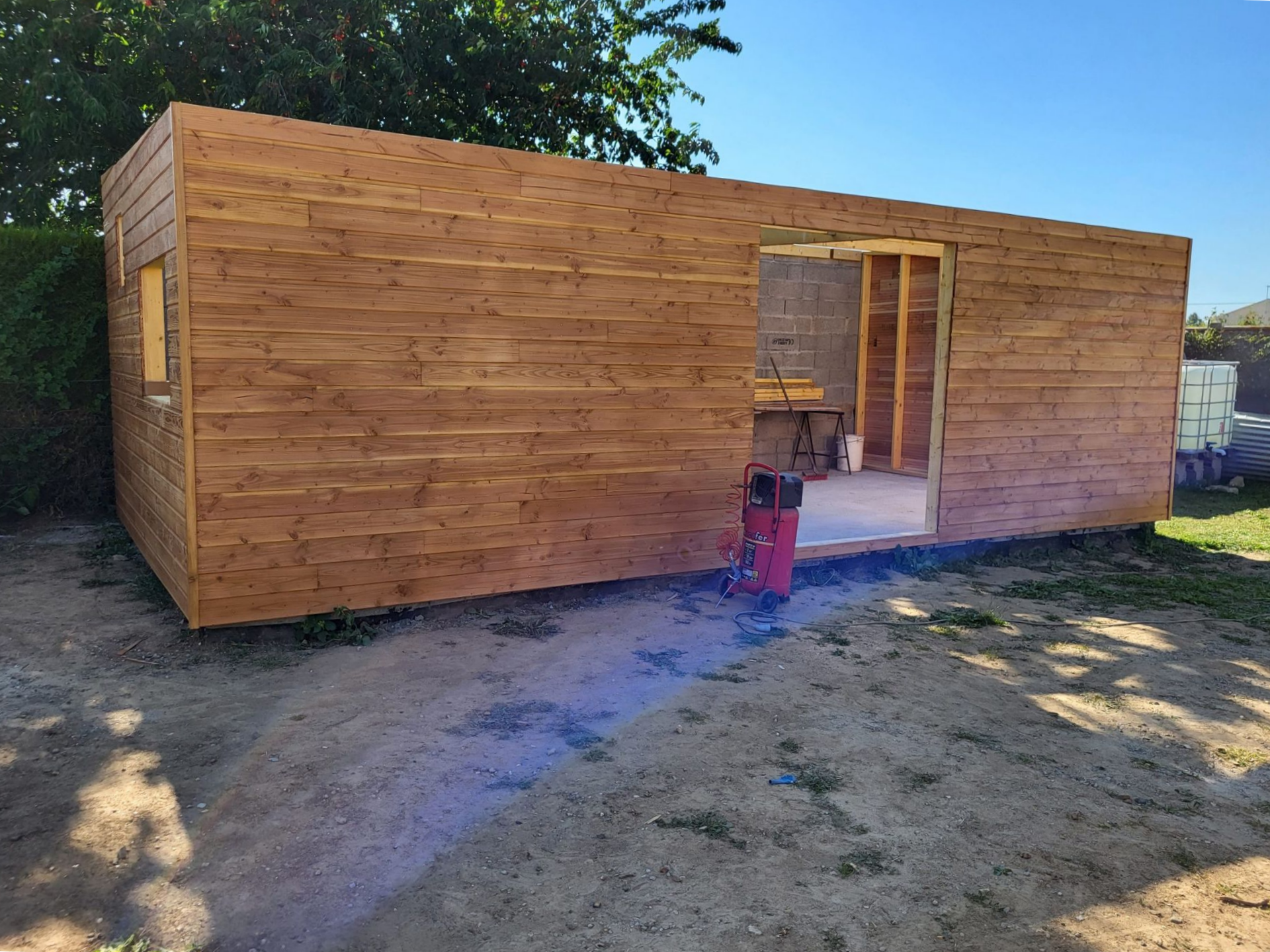 Abri de jardin en bois en construction à l'extérieur, avec porte ouverte et outils.