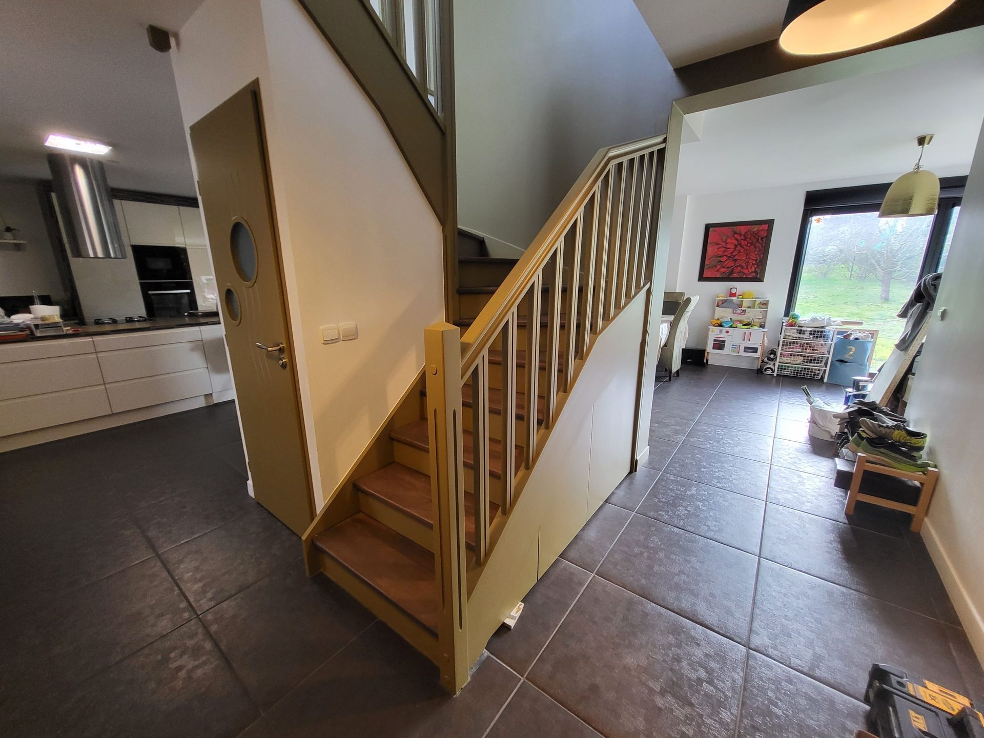 Escalier avec marches et rampe en bois menant à l'étage. Cuisine et séjour visibles.