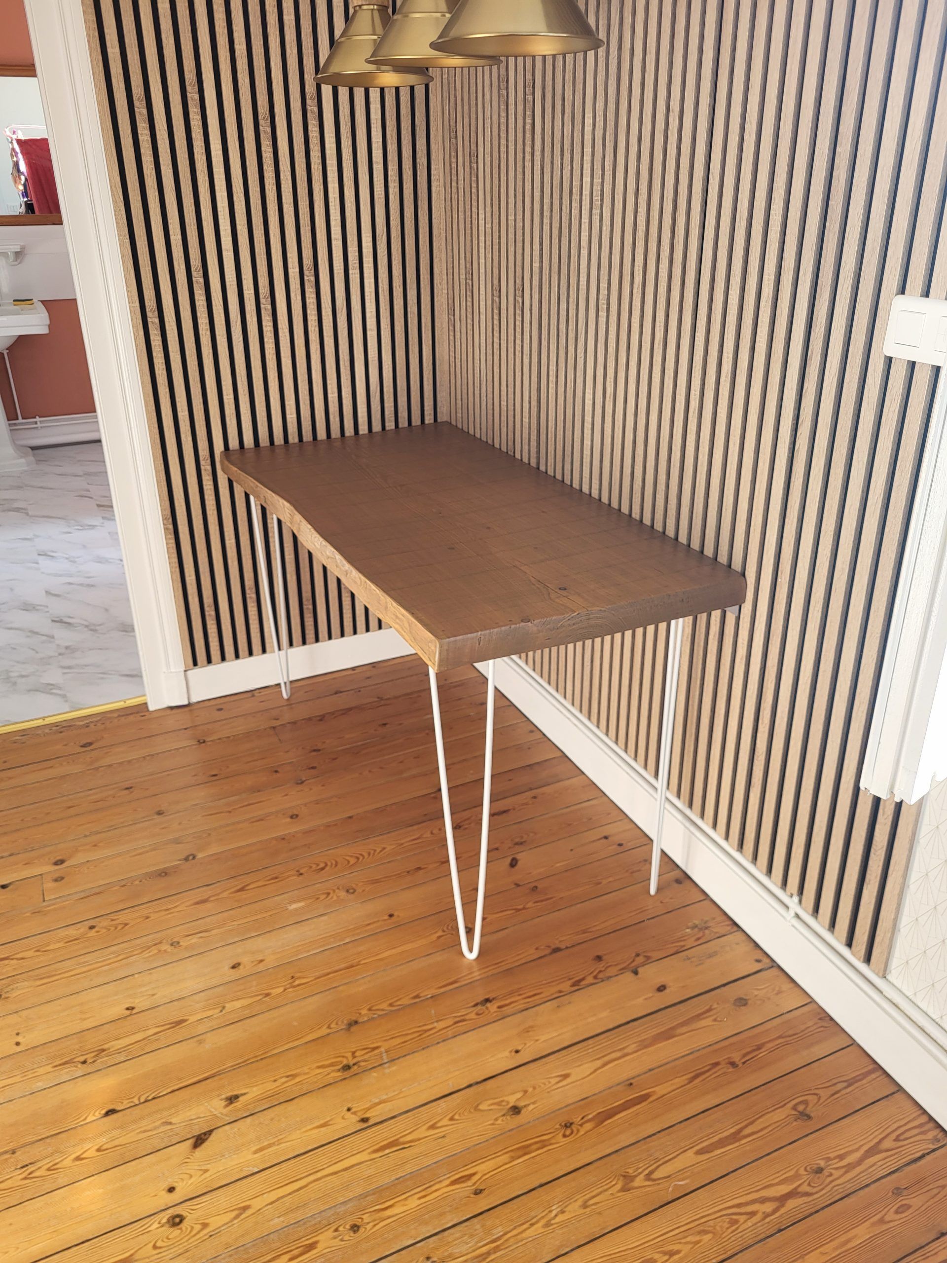 Table en bois à pieds d’épingle dans un coin, contre un mur rayé et un parquet.