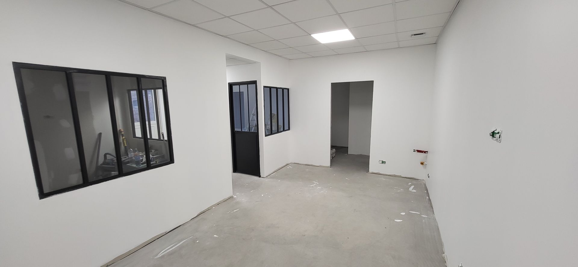 Vue intérieure d'une pièce blanche en construction, avec une fenêtre et des portes.