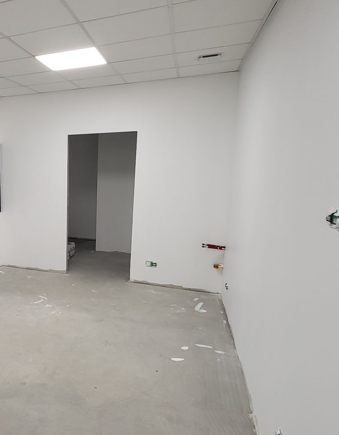 Intérieur d'une pièce aux murs blancs, avec une porte ouverte et un sol en béton en construction.