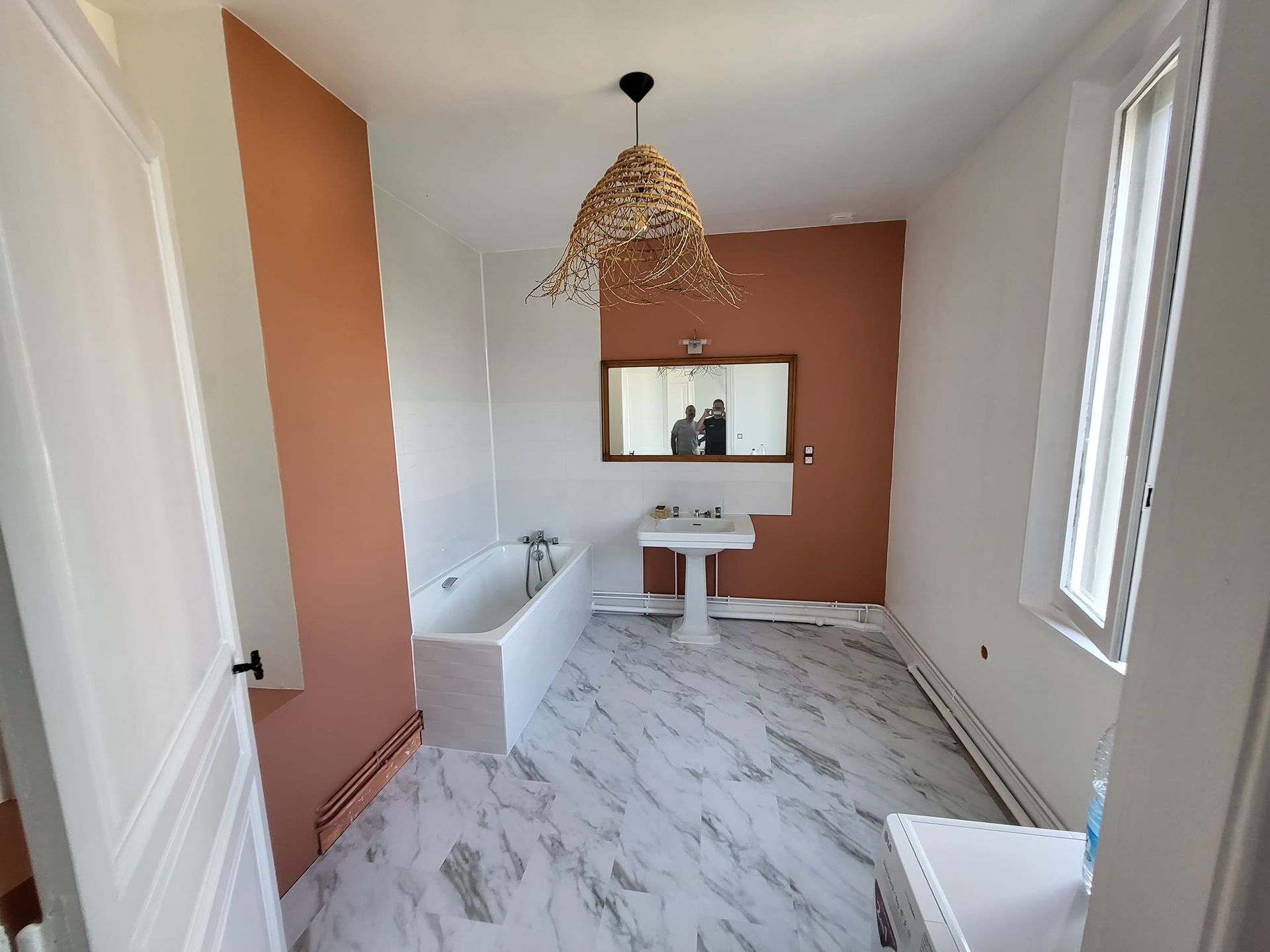 Salle de bains avec murs aux tons pêche, robinetterie blanche et sol imitation marbre. 