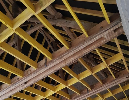 Charpente de toit en bois avec poutres jaunes, fond sombre et poutres de soutien apparentes.