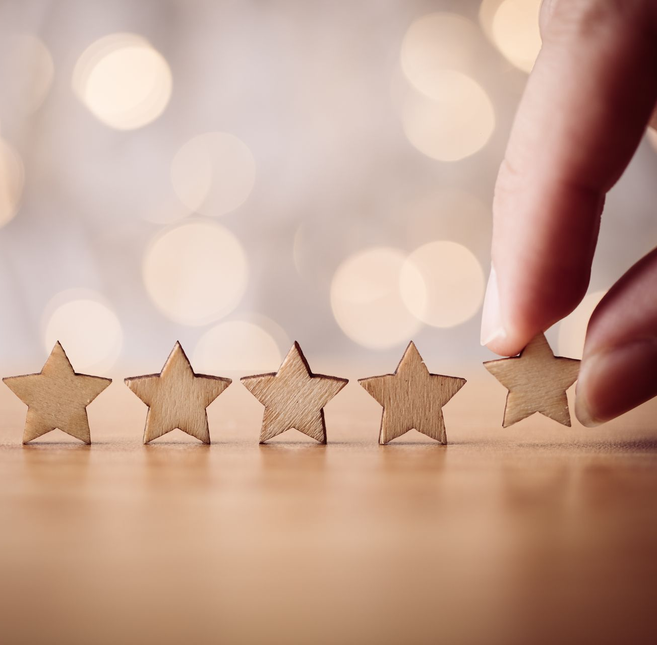 Une main pose une étoile en bois pour compléter une rangée de cinq étoiles sur une surface en bois, sur un fond doux.