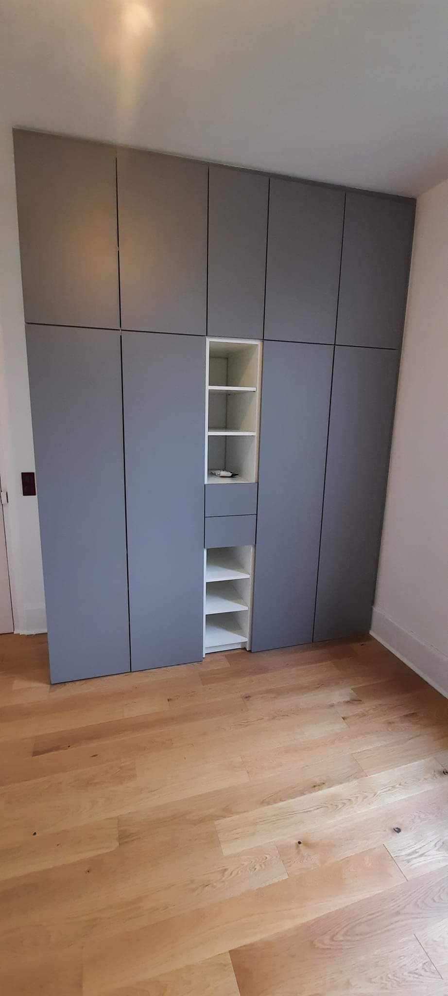 Placard intégré gris avec étagères ouvertes sur parquet.