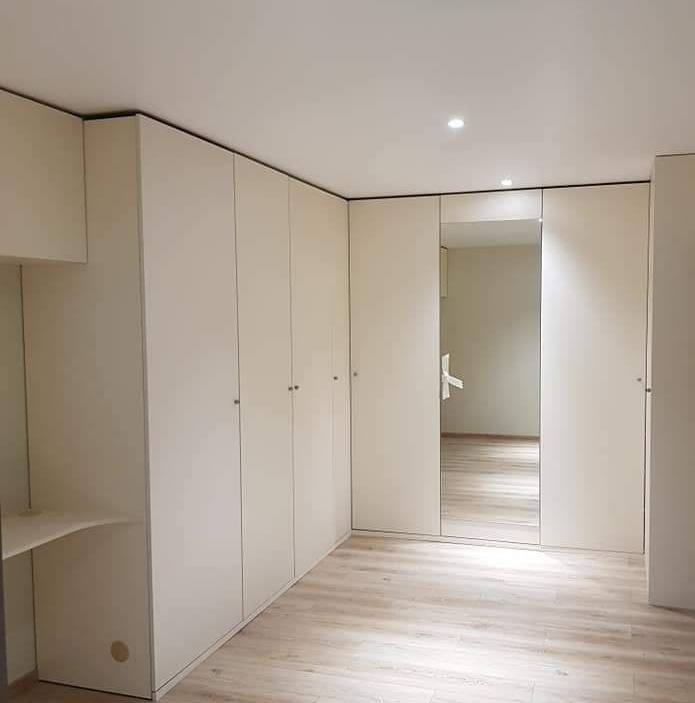 Placard intégré couleur crème avec plusieurs portes et une partie centrale en miroir, parquet clair, pièce lumineuse.