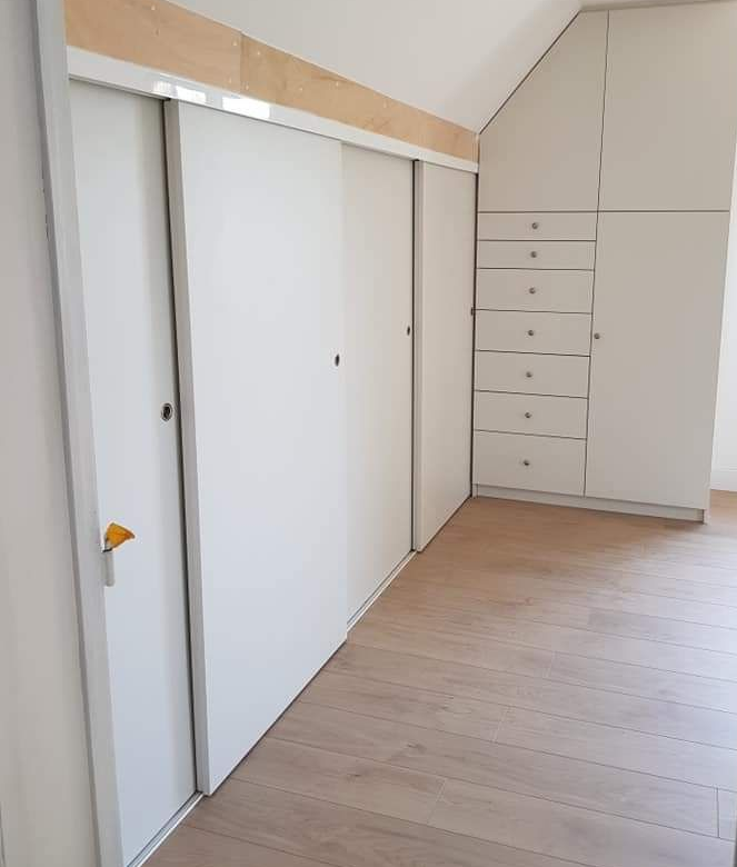 Portes et tiroirs de placard blancs intégrés dans un mur en angle, à côté d'un parquet clair.