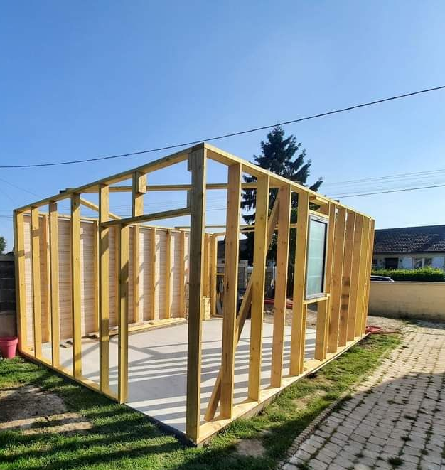 Construction d'une structure d'abri en bois à l'extérieur, avec une fenêtre et un environnement herbeux.