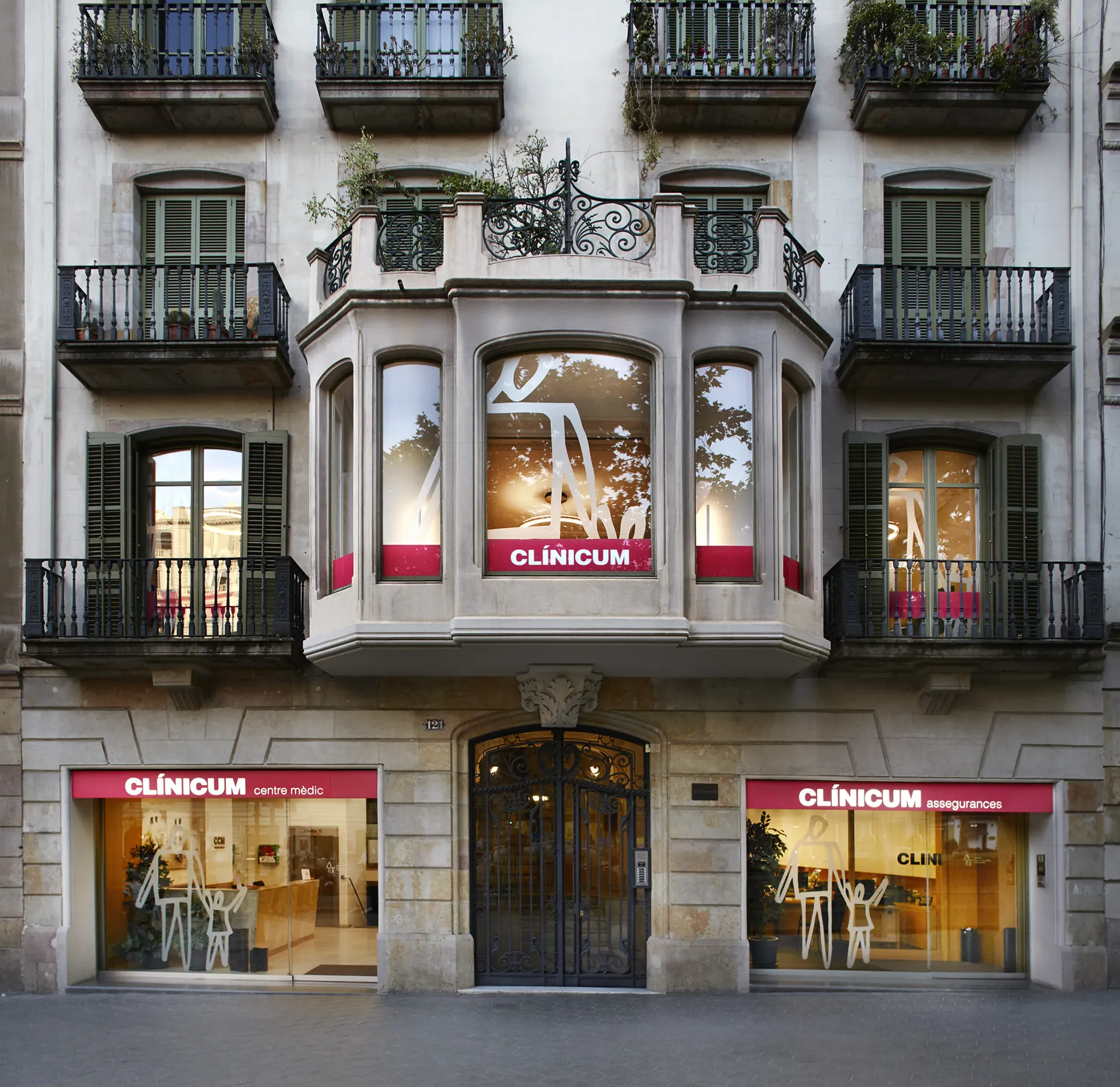 Fachada de un edificio con balcones ornamentados y escaparates, letrero de CLINICUM.