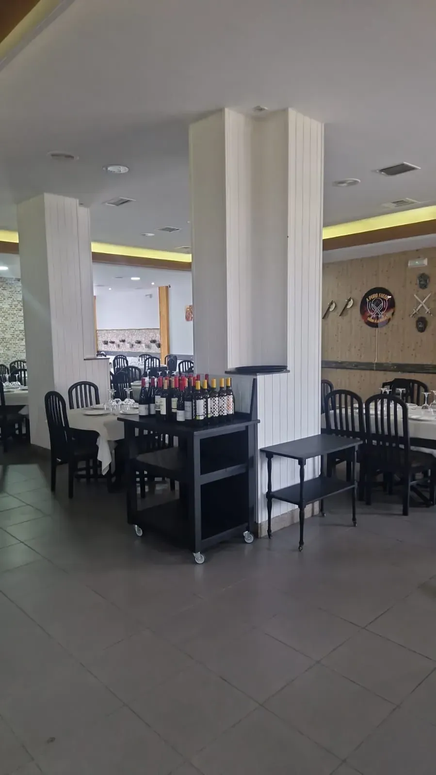 Comedor vacío de un restaurante con sillas negras, columnas blancas y una mesa de exposición central.