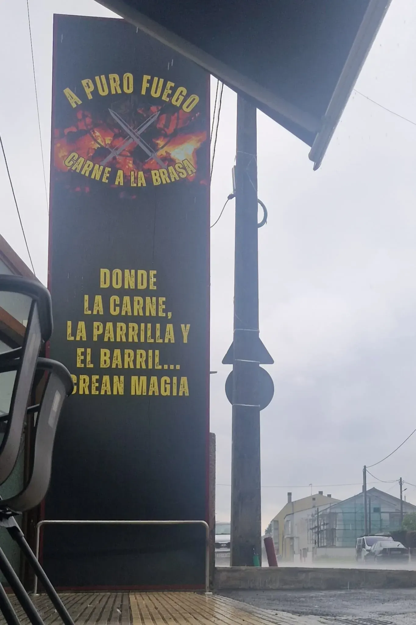 Letrero negro de “A Puro Fuego” con texto amarillo en una esquina de calle envuelta en niebla.