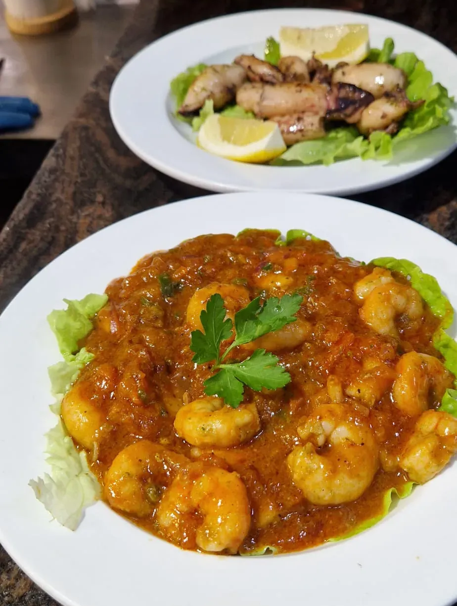 Dos platos servidos en una encimera oscura, que incluyen pollo en salsa y una ensalada verde con rodajas de lima.