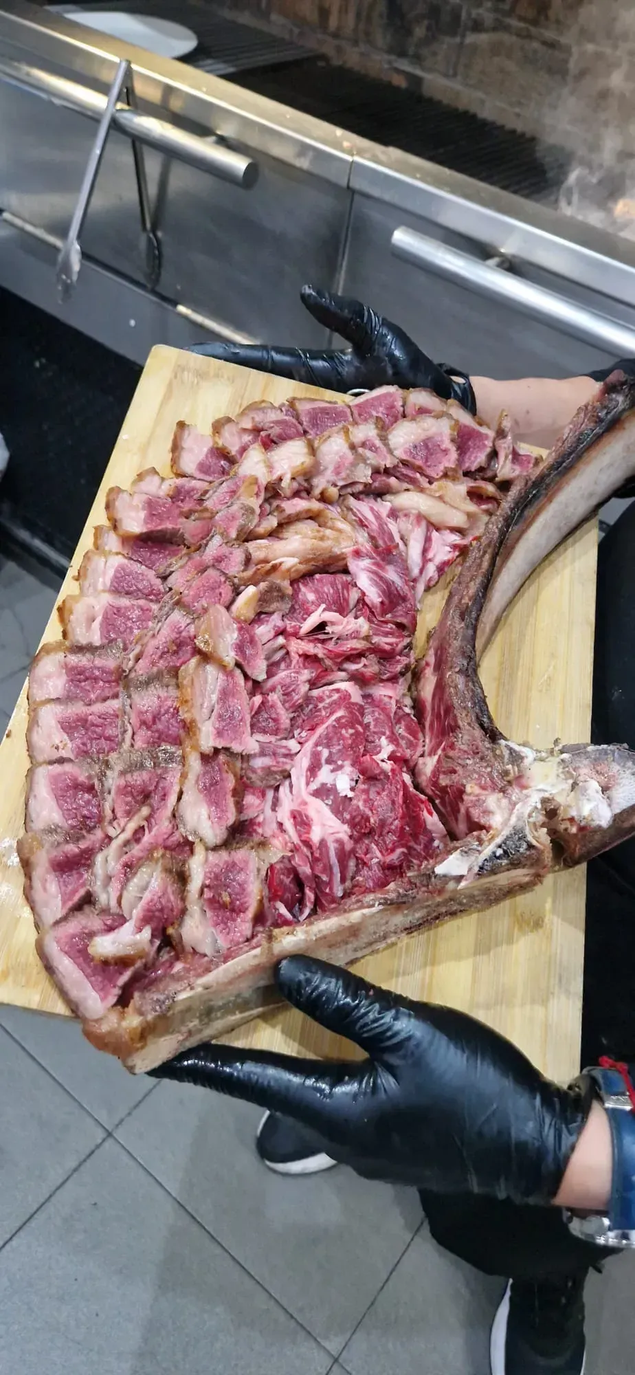 Manos enguantadas sosteniendo una bandeja de carne cruda en rodajas en el fregadero de la cocina.