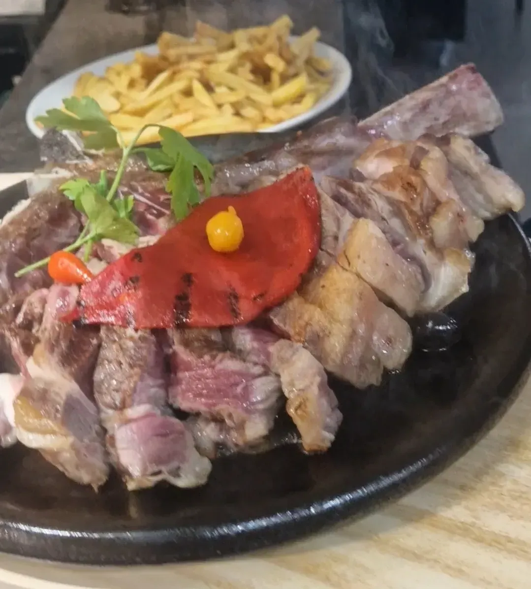 Plato de carne a la parrilla con guarnición y un tazón de papas fritas como acompañamiento.