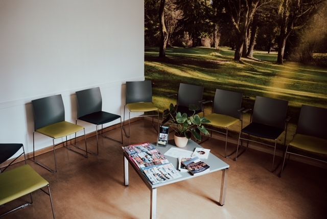 Ein Wartezimmer mit einem Tisch und Stühlen und einem Bild an der Wand.