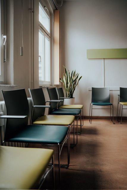 Eine Stuhlreihe in einem Wartezimmer mit einer Pflanze im Hintergrund.