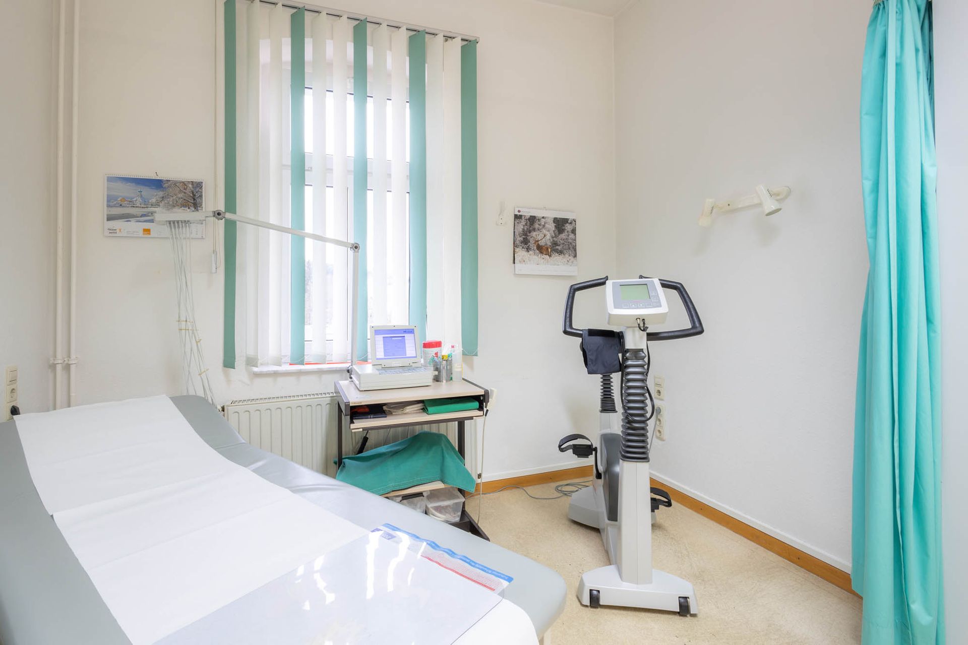 Eine Arztpraxis mit Bett, Schreibtisch und Heimtrainer.