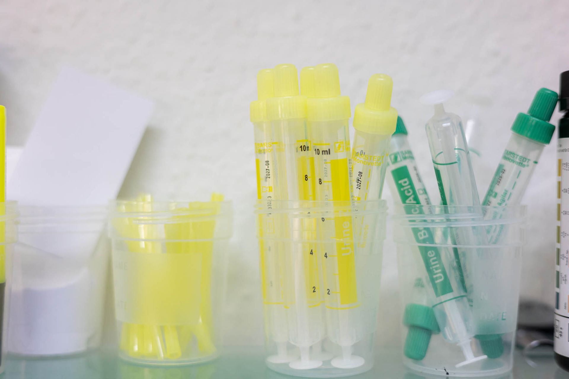 Eine Reihe von Plastikbechern gefüllt mit gelben Röhrchen und Spritzen auf einem Tisch.