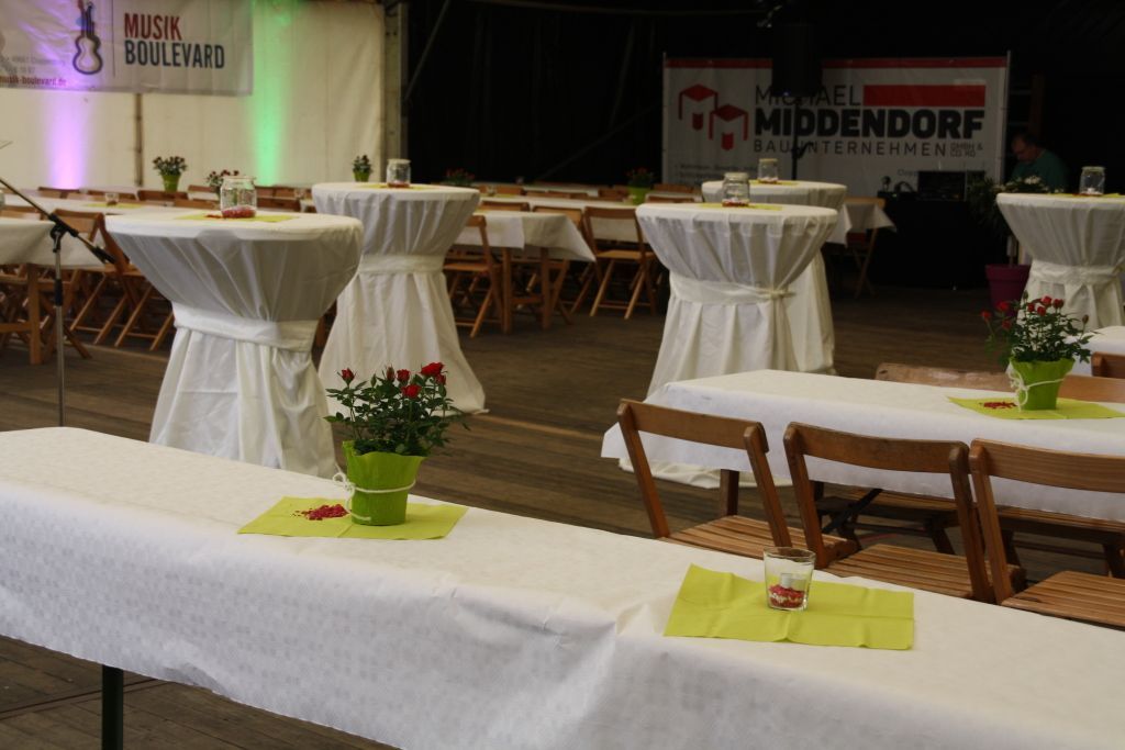Tische und Stühle sind für eine Party aufgestellt, im Hintergrund steht ein Schild mit der Aufschrift „Hiddendorf“