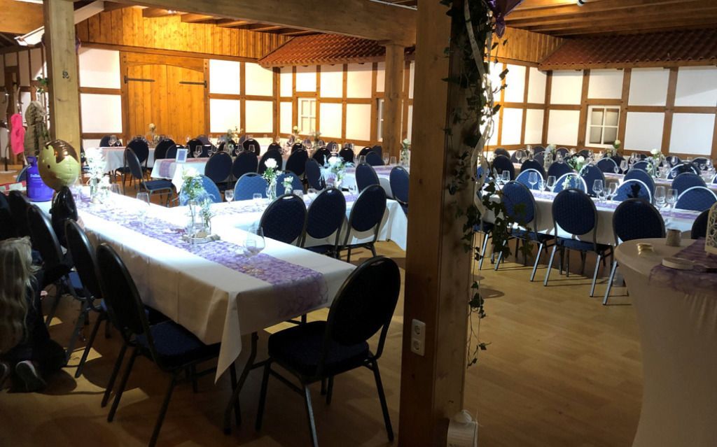 Ein großer Raum mit Tischen und Stühlen, aufgestellt für einen Hochzeitsempfang.