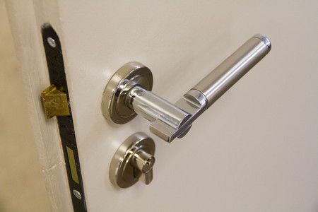 Gros plan sur une poignée et une serrure argentées d'une porte blanche, le loquet étant visible.