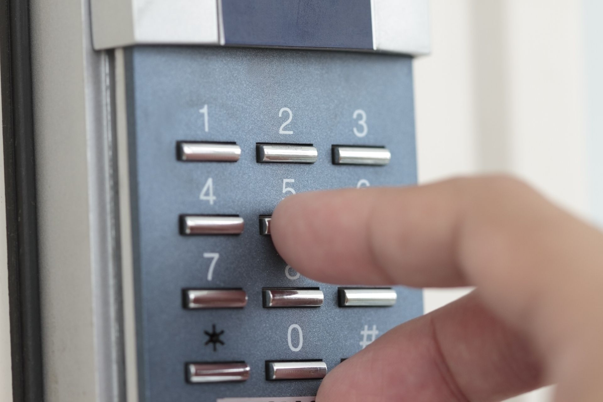 Une main appuie sur un chiffre sur un clavier métallique à chiffres blancs et écran rétroéclairé