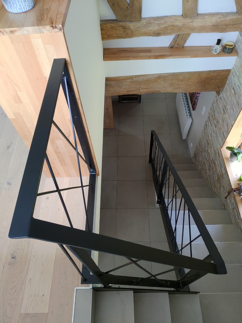Escalier intérieur avec rampe en métal noir et sol carrelé beige, vu du dessus.