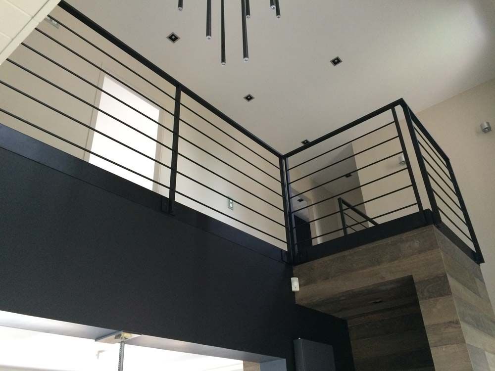 Intérieur moderne avec balcon à l'étage, rambarde en métal noir et plafond incliné.