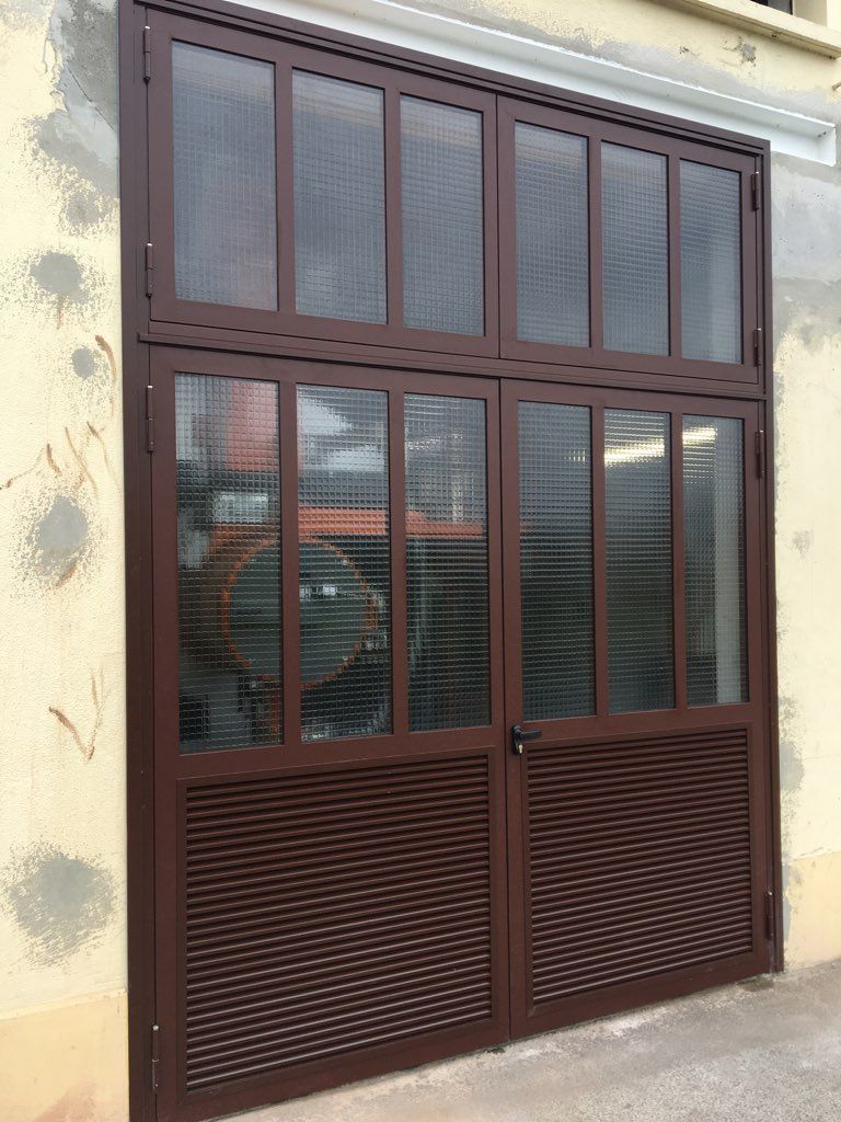 Porte double vitrée à cadre métallique brun et panneaux grillagés sur un mur beige