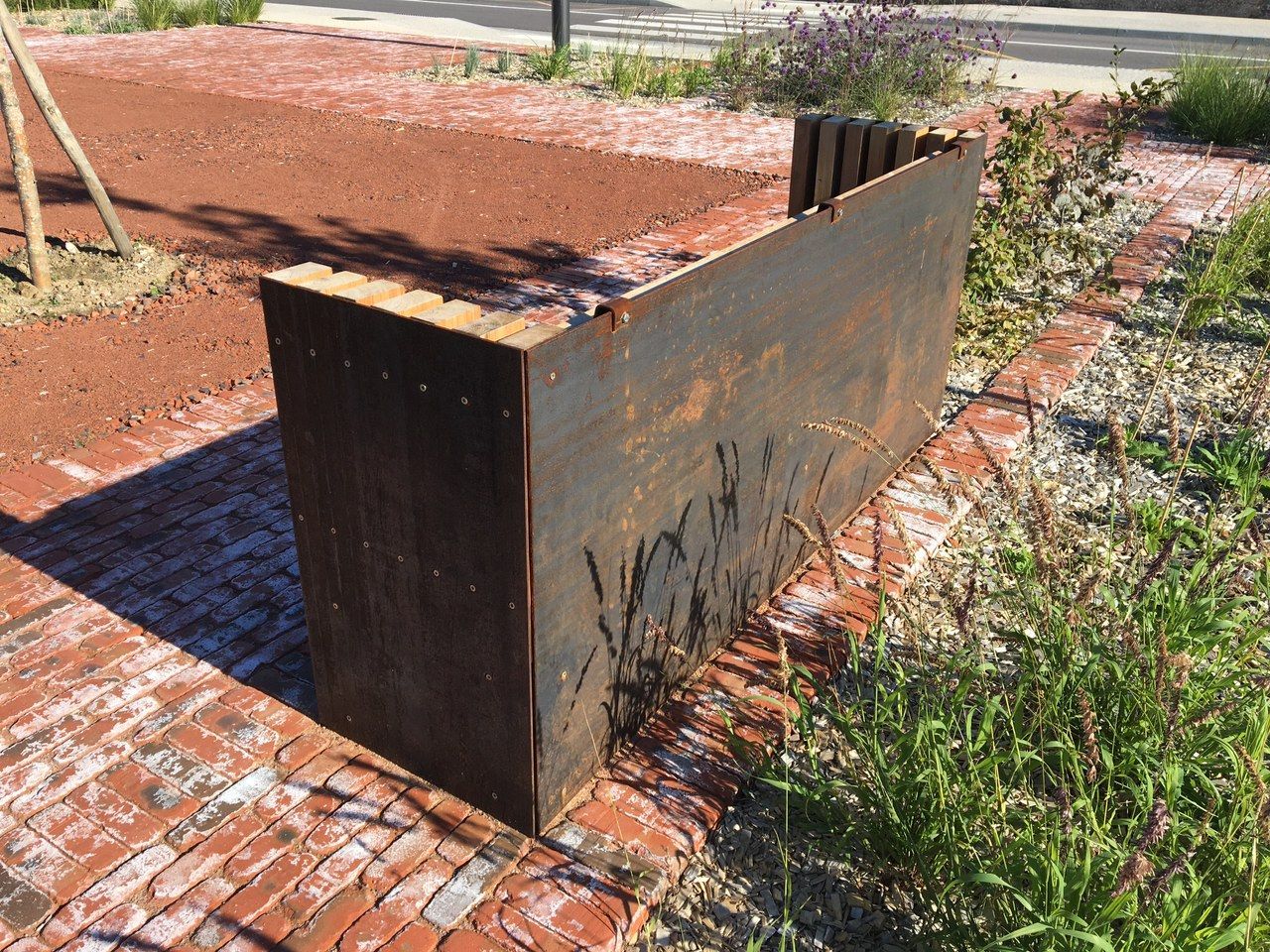 Sculpture de banc en métal rouillé au bord d'un chemin de briques dans un jardin paysager