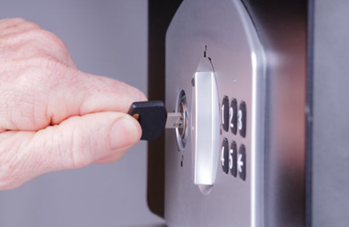 Main insérant une clé dans une serrure de coffre-fort à combinaison argentée, les boutons du clavier à proximité