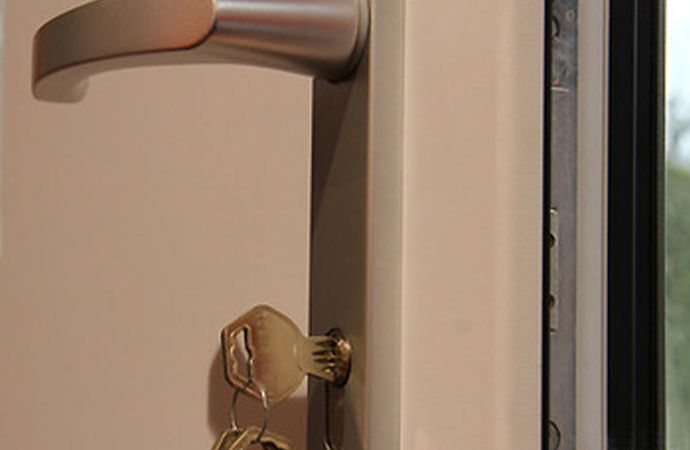 Gros plan sur une poignée de porte en métal et une clé dans une serrure sur un cadre de porte beige.