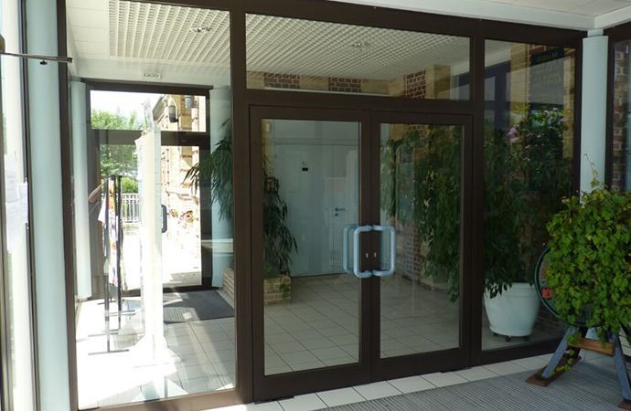 Portes d'entrée vitrées donnant sur un bâtiment avec des plantes en pot et une allée couverte