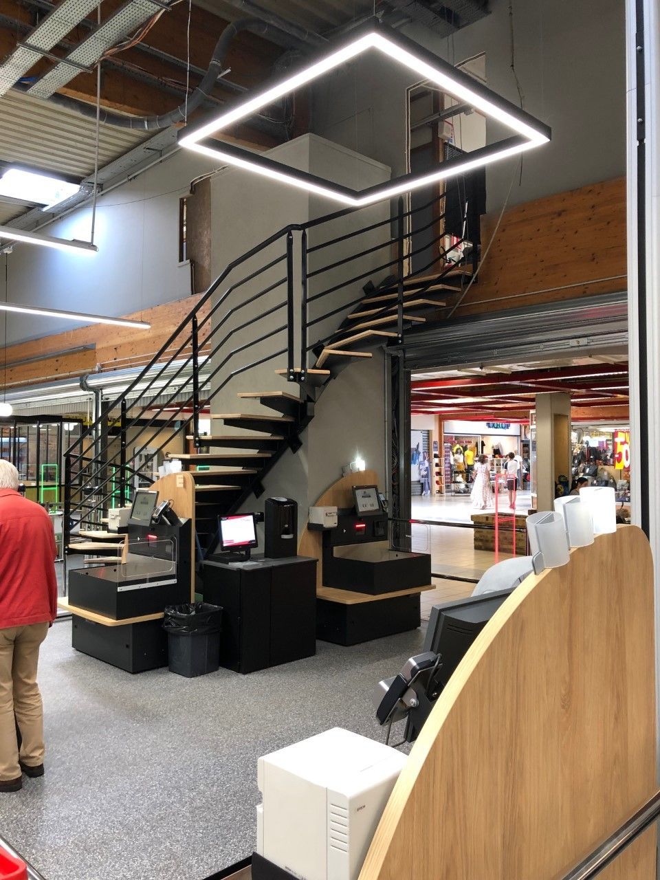 Escalier intérieur moderne avec rampes noires dans un magasin, sous un plafonnier carré lumineux