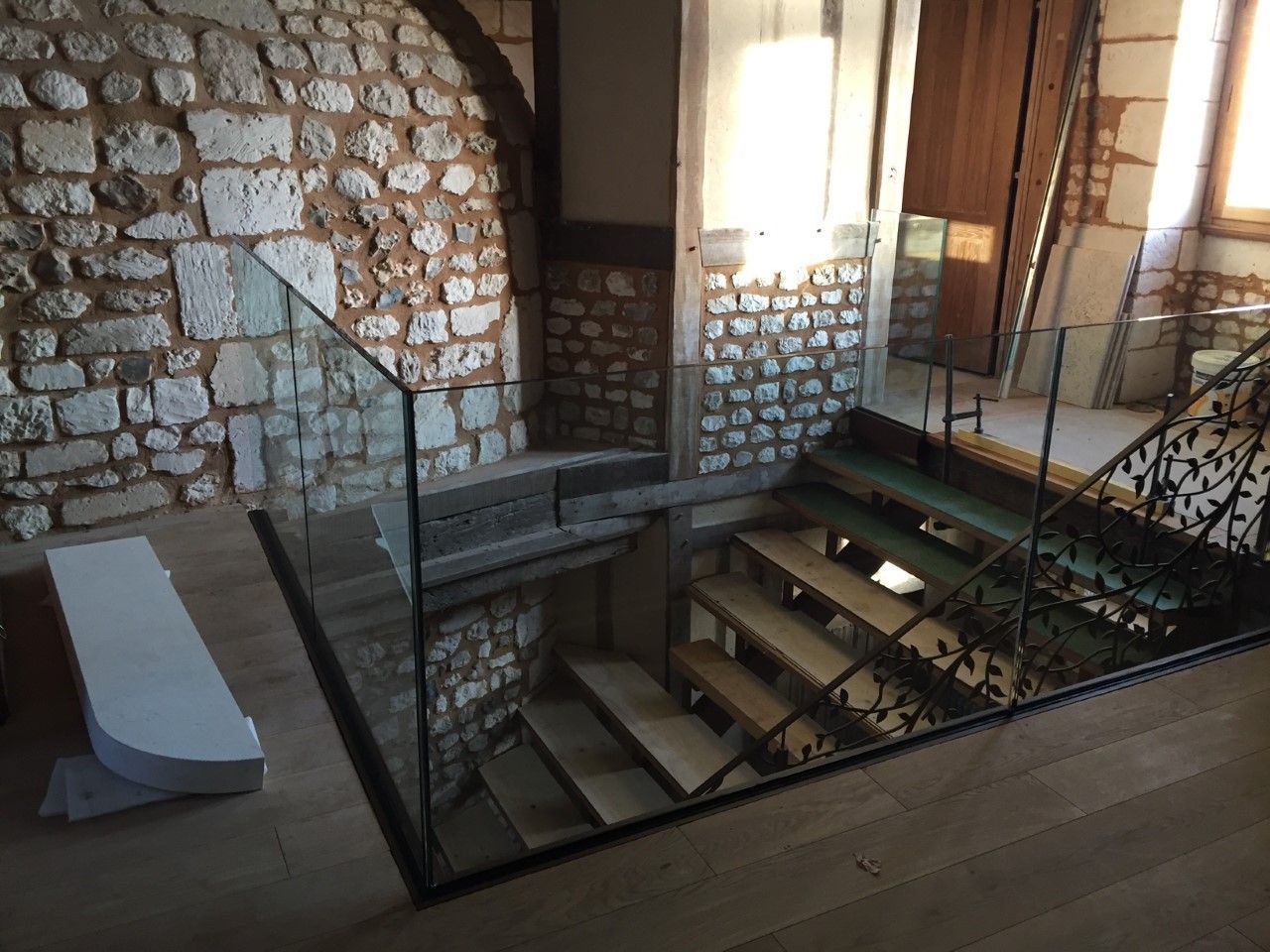 Intérieur en pierre avec un escalier ouvert, une balustrade en verre et un banc blanc près d'une fenêtre ensoleillée.