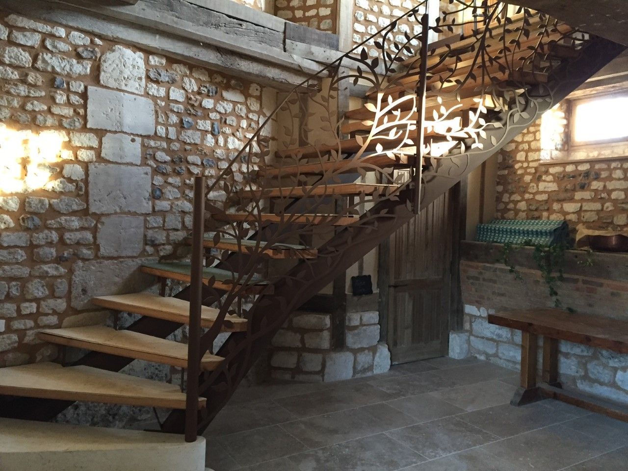 Escalier en pierre avec marches en bois dans une pièce rustique, à côté d'un banc et de murs en pierre.